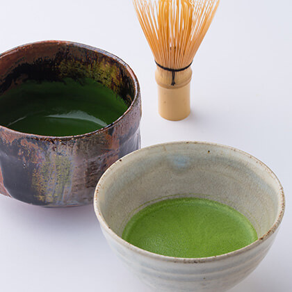 Two bowls of matcha tea with a whisk